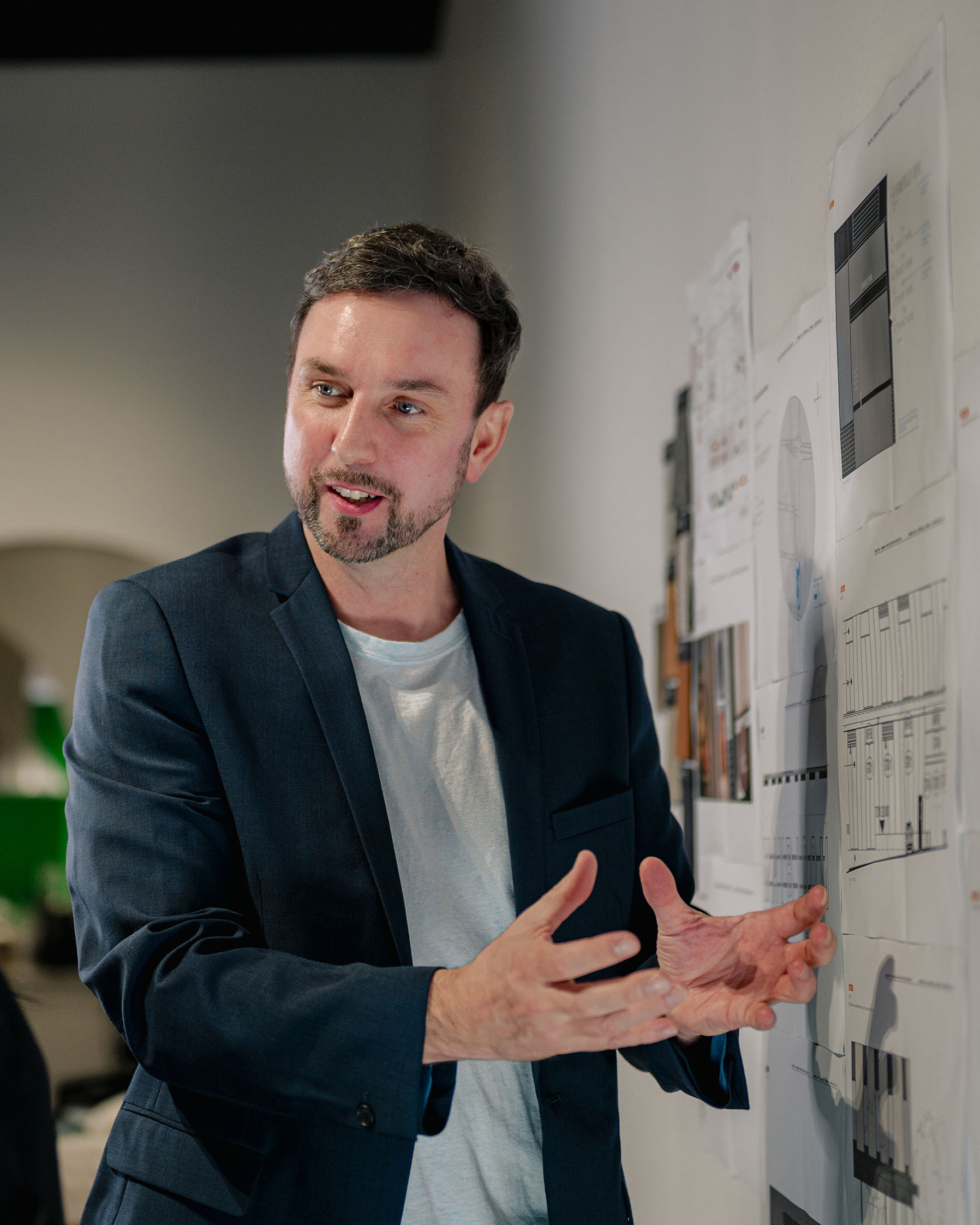 Micio's director, Thomas, standing in front of a wall of sketches and design documentations, explaining something to another person.