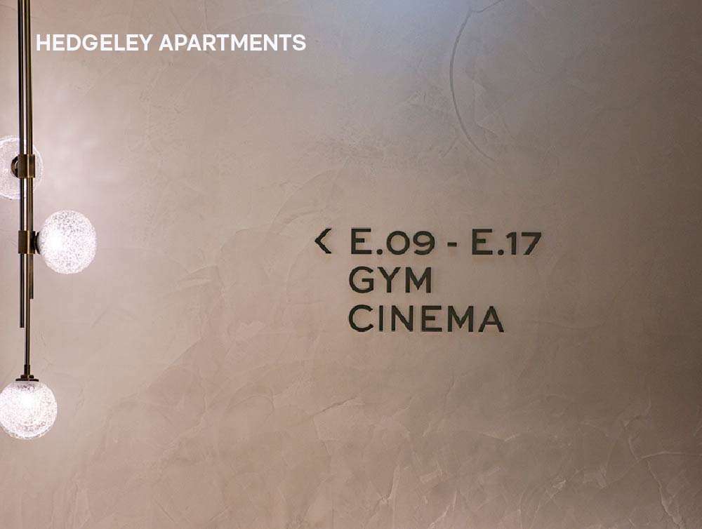 Wayfinding signage at Hedgeley Apartments that has brown directional text on light grey wall.