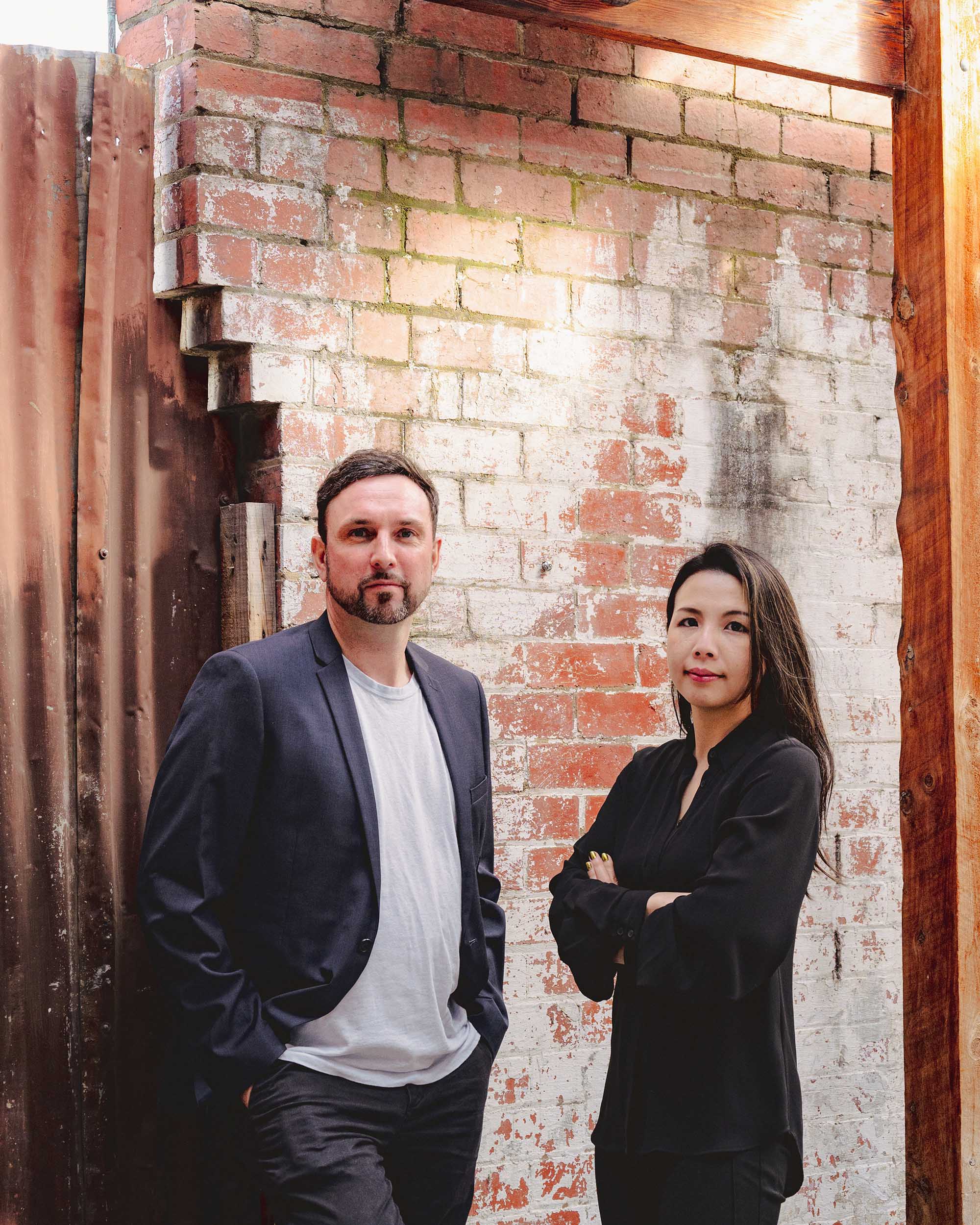 Micio's two directors, clare and Thom, standing in front of a brick wall.